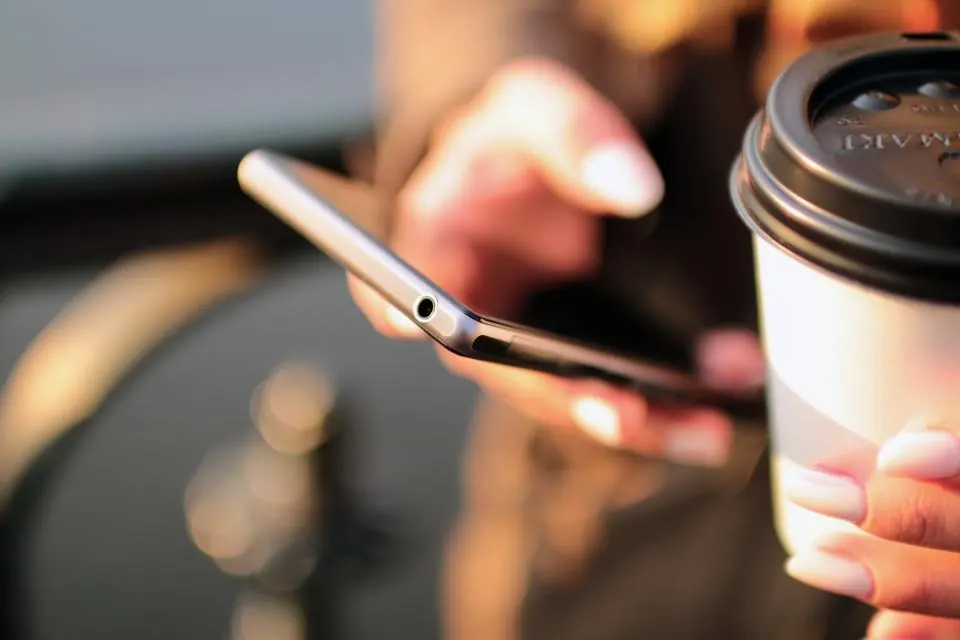 A client booking an appointment on a smartphone with a coffee in hand